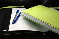 Picture of closed notebook on top of open manuscript and two pens